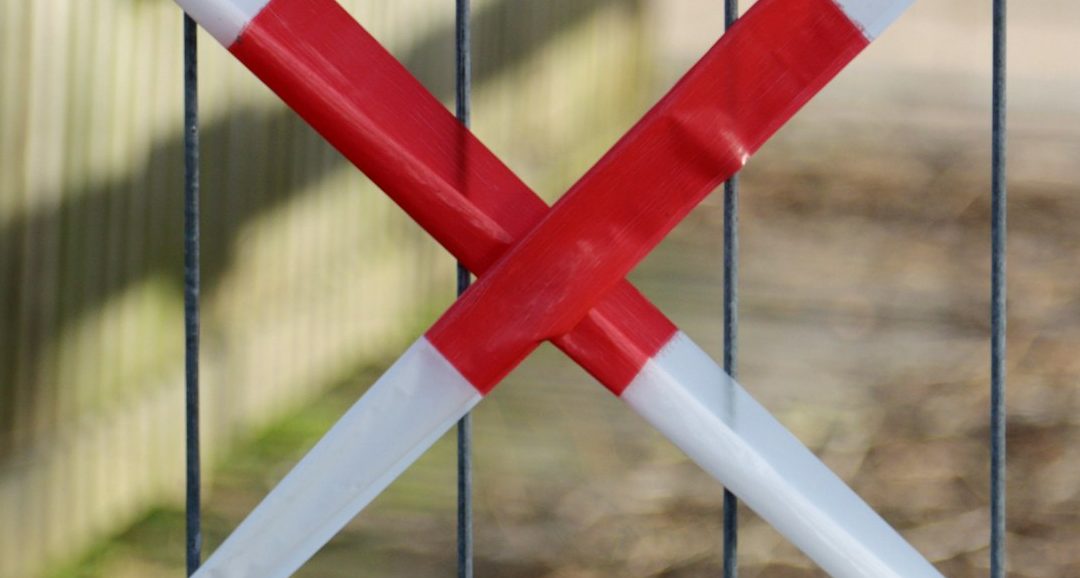 Rotes und weißes Absperrband in Form eines Kreuzes, umgeben von einem Zaun.