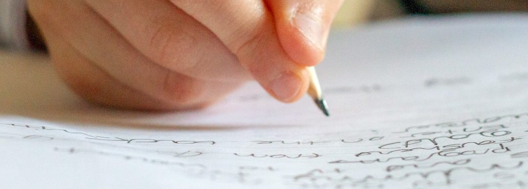 Eine Hand hält einen Bleistift und schreibt auf ein Blatt Papier mit Notizen.