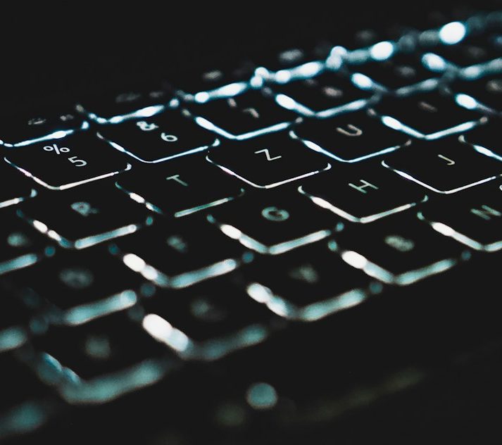 Nahaufnahme einer beleuchteten Computertastatur auf dunklem Hintergrund.